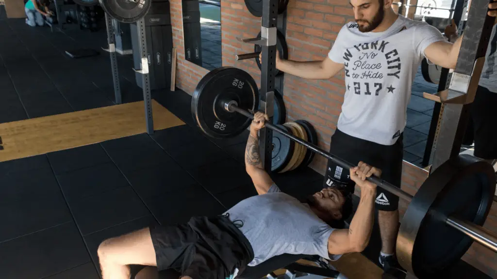 Man doing bench presses with the help of his trainer