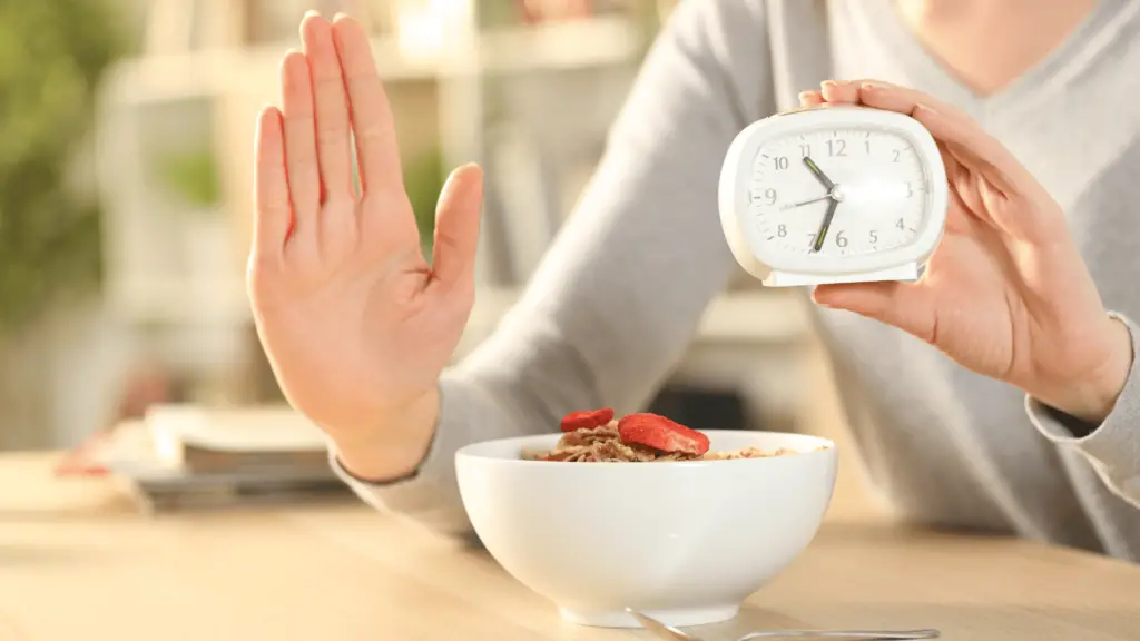 Woman showing stop sign and holding a clock, representing intermittent fasting