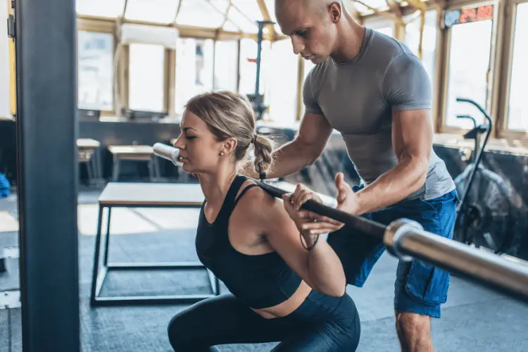 Woman doing weighted squats with the help of her trainer