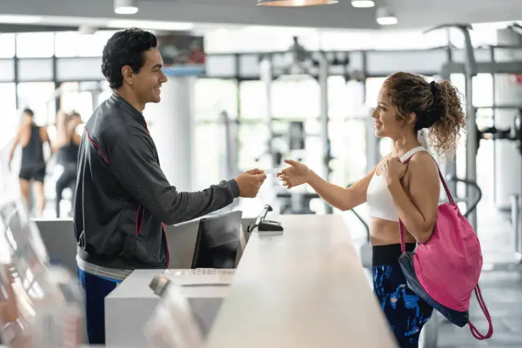 A cheerful employee handing a gym membership card to a young woman in the gym 