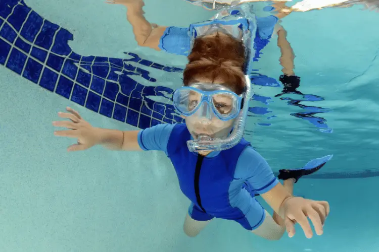 Child swimming underwater in pool wearing swimming goggles