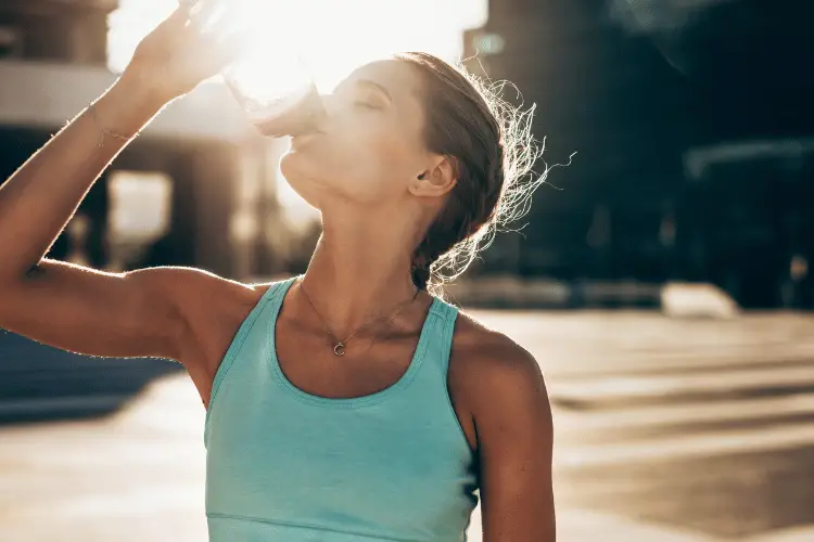 Fit young woman drinking water after exercising in hot temperature